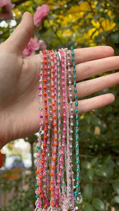 a hand is holding several bracelets with beads on it and flowers in the background