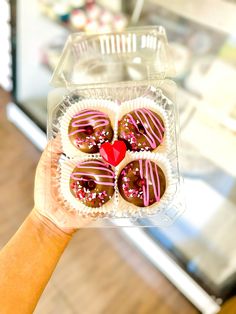 a hand holding a plastic container filled with chocolate covered donuts