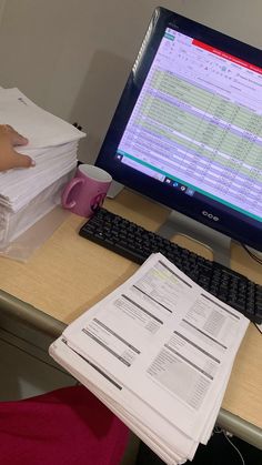 a computer monitor sitting on top of a desk next to a pile of papers and a keyboard