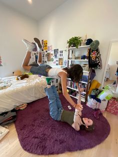 two people laying on the floor in a room with bookshelves and purple rugs