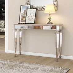 a silver console table with two framed pictures on top and a lamp next to it