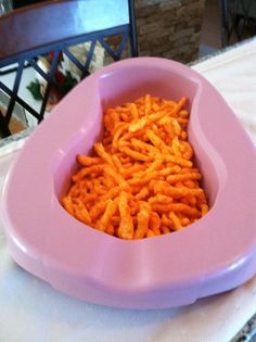 a pink bowl filled with cheetos sitting on top of a white tablecloth