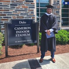 a man wearing a cap and gown standing in front of a sign