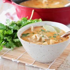 a bowl of soup on a place mat next to a pot of soup and a wooden spoon