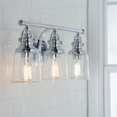 three light bathroom fixture with clear glass shades on the wall and white tile behind it