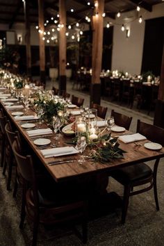 a long wooden table with place settings and candles on the tables in front of it