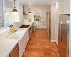 a kitchen with white cabinets and brown tile flooring, along with stainless steel appliances