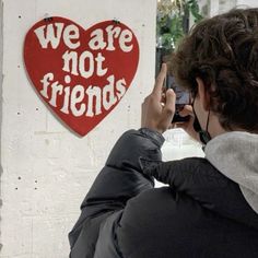 a person taking a photo with their cell phone in front of a sign that says we are not friends