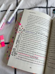 an open book sitting on top of a bed next to markers