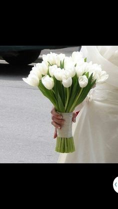 a bride holding a bouquet of white tulips in her hand while walking down the street