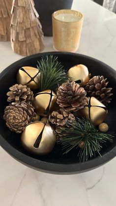 a black bowl filled with pine cones and gold ornaments on top of a white table