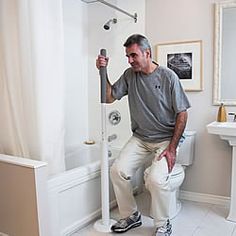 a man sitting on top of a toilet next to a white sink and shower head