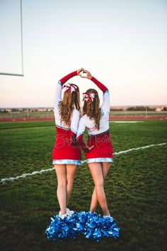 two cheerleaders standing in the middle of a field with their hands on their heads