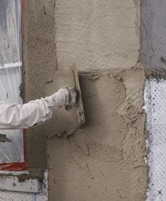 a man wearing a white suit and tie standing in front of a window holding onto the side of a building