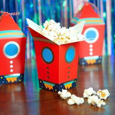 three red boxes filled with popcorn sitting on top of a wooden table next to candy