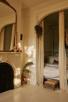 a bed sitting next to a fire place in a living room under a mirror on top of a wooden floor