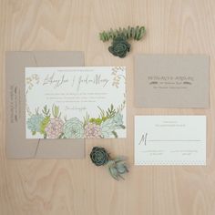 wedding stationery with succulents and greenery on wooden table next to flowers