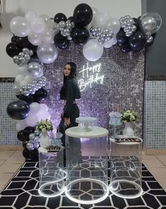 a woman standing in front of a table with balloons and decorations on the wall behind her