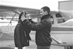 a man and woman standing in front of an airplane taking pictures with their cell phones