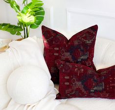 two red pillows sitting on top of a white bed next to a potted plant