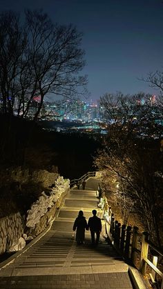 two people are walking down the stairs in the night with city lights on behind them