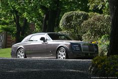 a rolls royce parked on the side of a road in front of trees and bushes