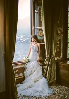 a woman in a wedding dress standing by a window