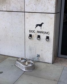 the dog parking sign is on the side of the building with two bowls in front of it