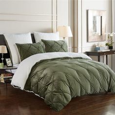 a bed with green comforter and pillows on top of it next to a night stand