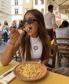 a woman sitting at a table eating pasta from a plate with her mouth wide open