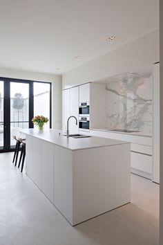 a kitchen with an island counter, sink and oven in the center is white marble