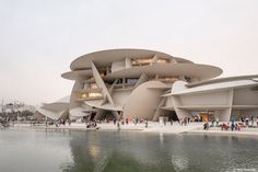 people are walking around in front of a building that is shaped like a boat on the water