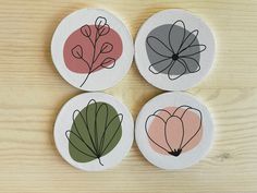 four coasters with different designs on them sitting on a wooden surface, one has a leaf and the other has a flower