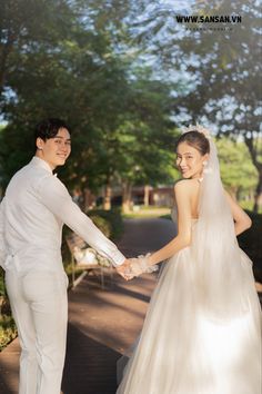 a bride and groom are holding hands on the sidewalk in front of some green trees