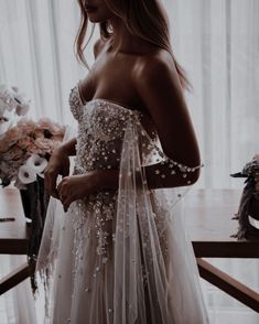 a woman in a wedding dress standing by a window