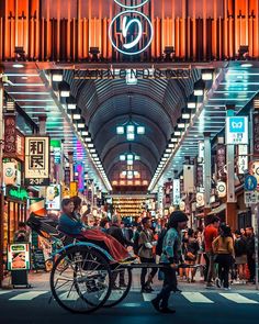 people are walking through an indoor market with many lights and signs on the ceiling,