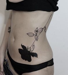 a woman's stomach with a black flower tattoo on her left side ribcage