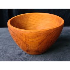 a wooden bowl sitting on top of a gray tablecloth covered floor next to a black wall