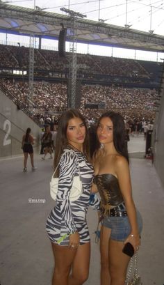 two beautiful young women standing next to each other in front of a stadium full of people