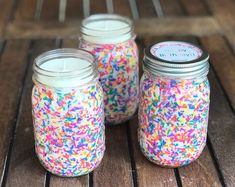 three mason jars filled with sprinkles on top of a wooden table