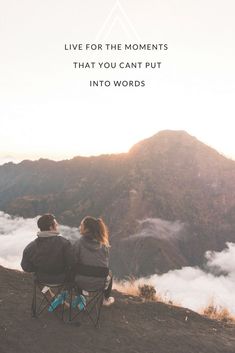 two people sitting on top of a mountain looking out at the clouds and mountains in the distance