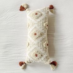 an embroidered pillow with tassels and pom poms on the bottom is laying on a white sheet