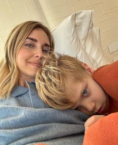 a woman laying on top of a bed next to a boy wrapped in a blanket