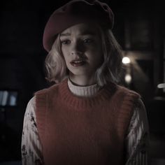 a woman with blonde hair wearing a red hat and sweater in a dimly lit room