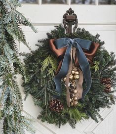 a christmas wreath hanging on the side of a white door with blue ribbon and bells