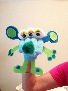 a woman holding up a knitted toy with eyes on it's face and hands