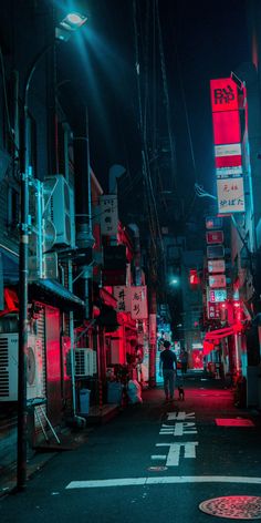 an alleyway with red lights and signs on the buildings at night time, along with a man walking down the street