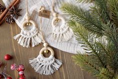 three white tasseled earrings hanging from strings on a table next to pine cones and cinnamon sticks