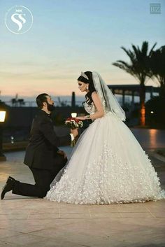 a man kneeling down next to a woman in a wedding dress