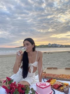 a woman sitting at a table with a cake and wine in front of her on the beach